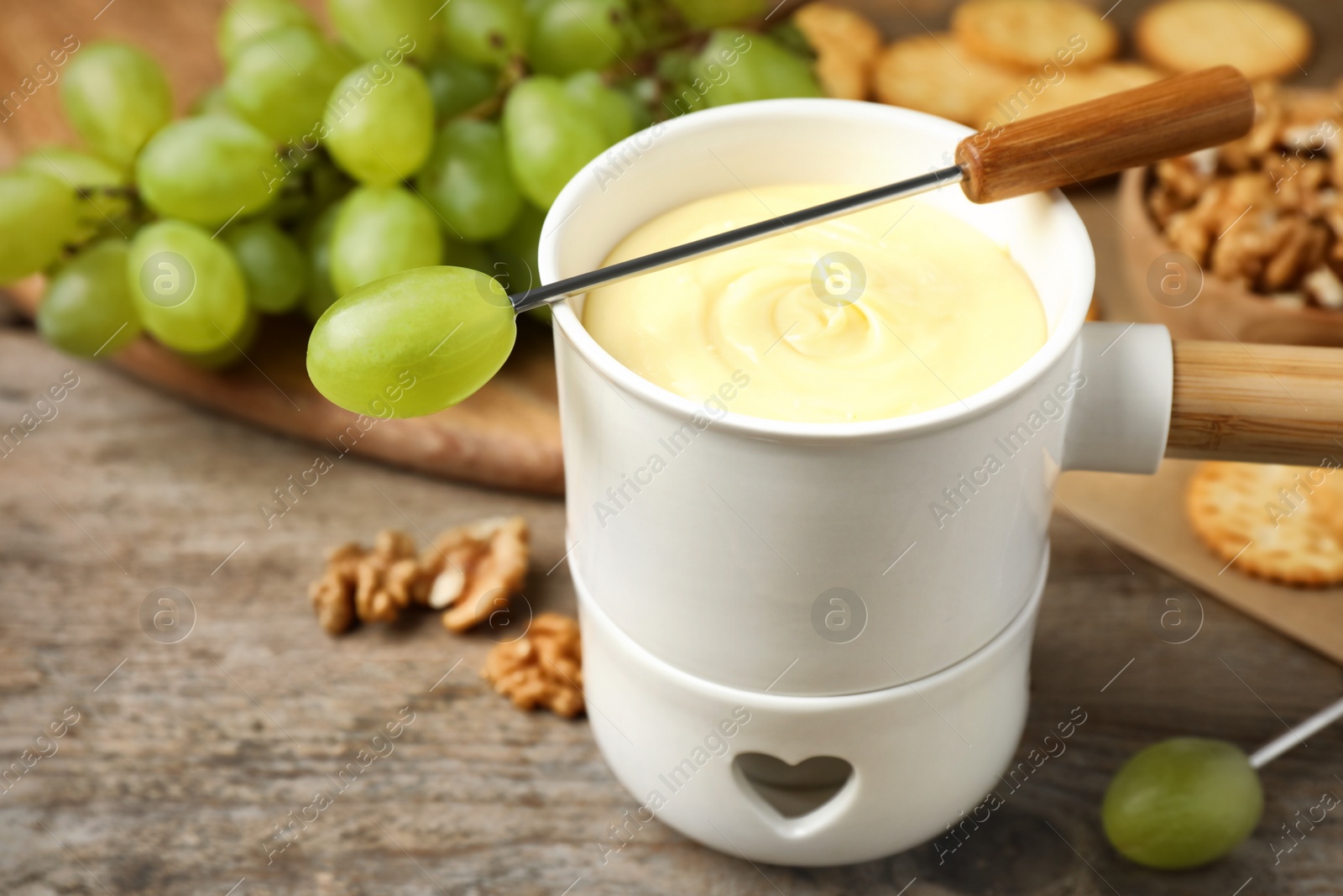 Photo of Fondue pot with white chocolate and grapes on wooden table, closeup