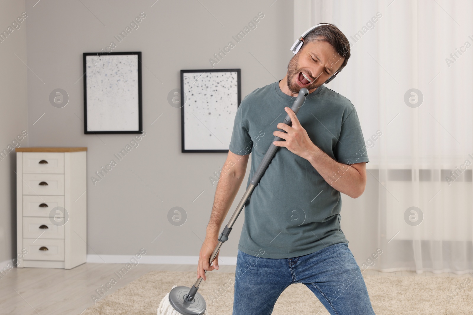 Photo of Enjoying cleaning. Happy man with mop singing while tidying up at home, space for text