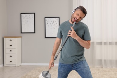 Photo of Enjoying cleaning. Happy man with mop singing while tidying up at home, space for text