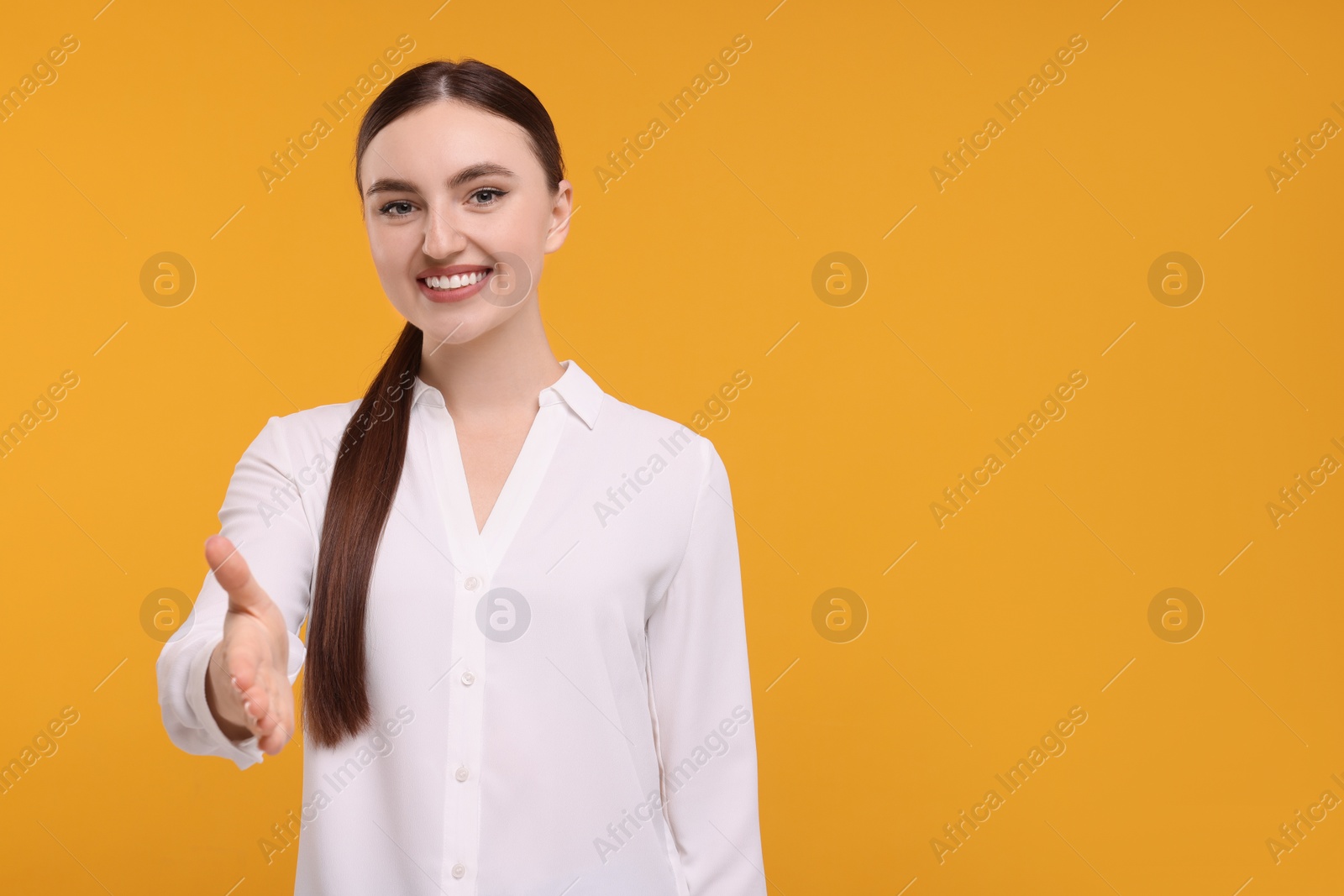 Photo of Smiling woman welcoming and offering handshake on orange background. Space for text