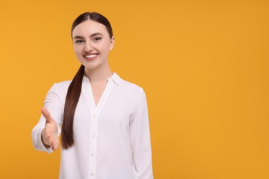 Photo of Smiling woman welcoming and offering handshake on orange background. Space for text