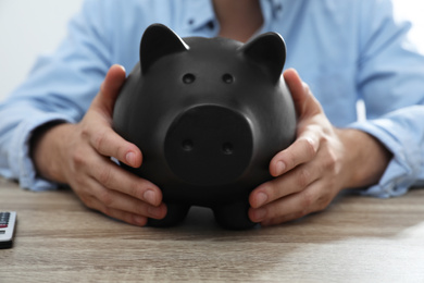 Photo of Man with piggy bank at wooden table, closeup