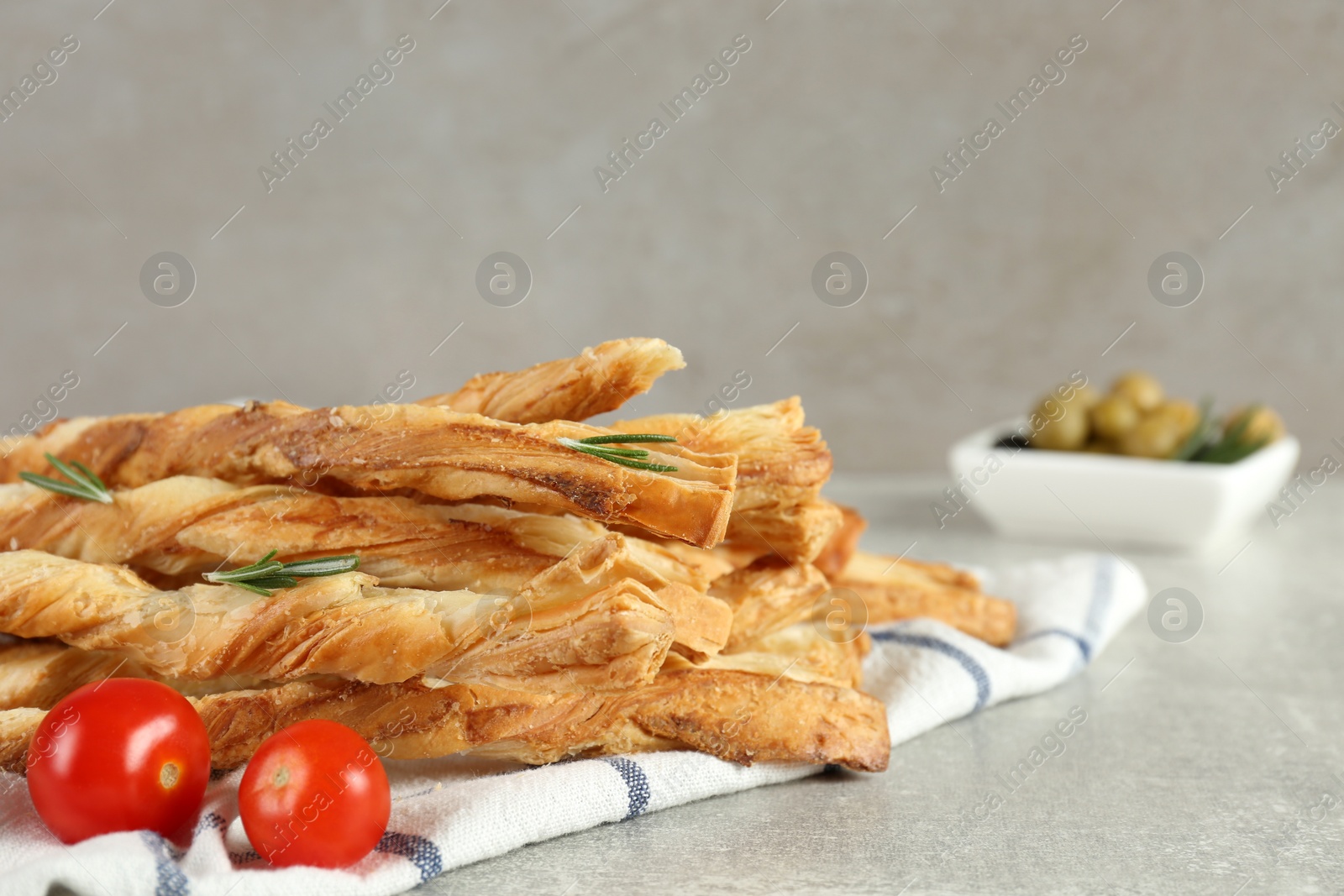 Photo of Fresh delicious grissini with rosemary and tomatoes on light grey table. Space for text