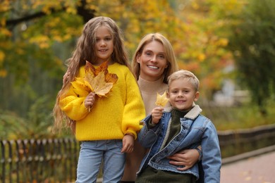 Portrait of happy mother and her children with dry leaves in autumn park