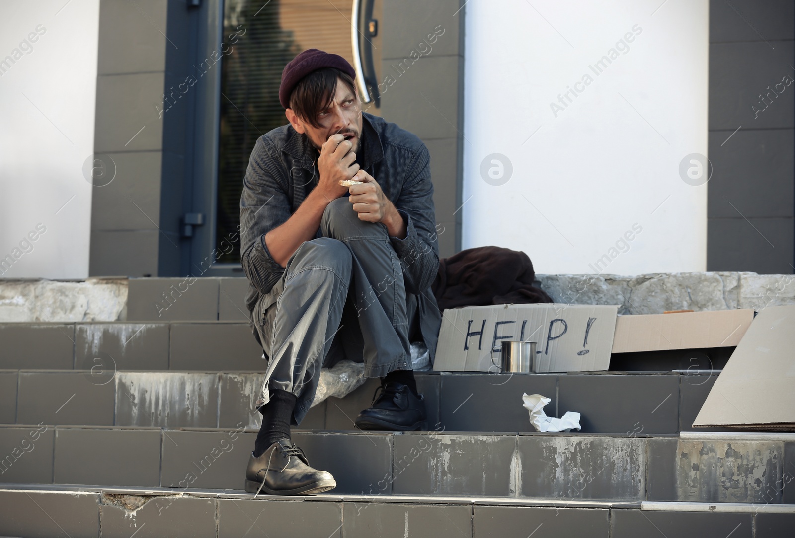 Photo of Poor homeless man eating piece of bread on city street