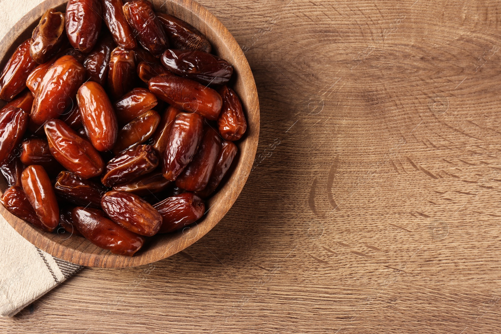Photo of Tasty sweet dried dates in bowl on wooden table, top view. Space for text