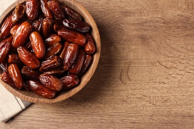 Tasty sweet dried dates in bowl on wooden table, top view. Space for text