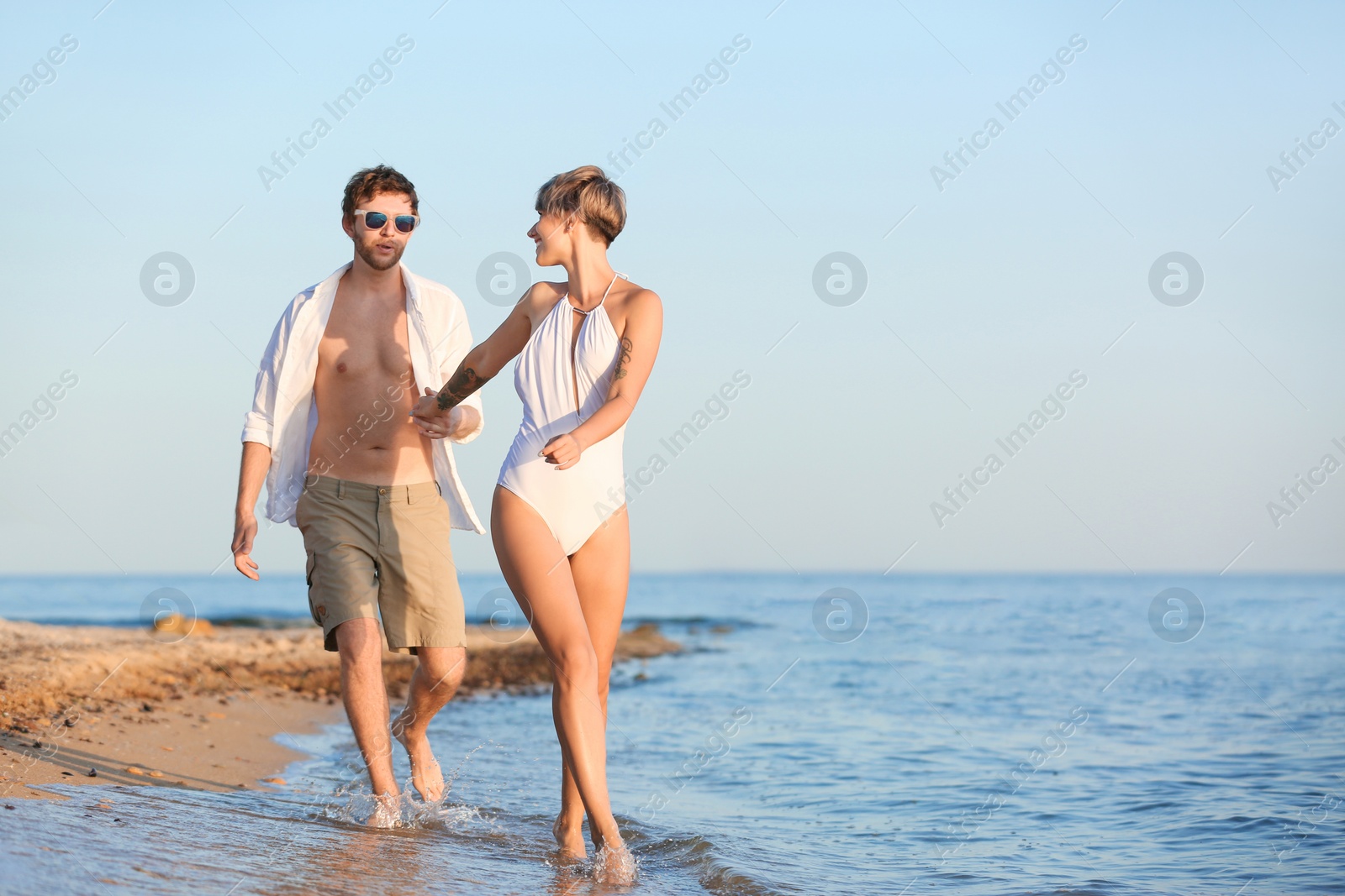 Photo of Happy young couple walking together on beach. Space for text