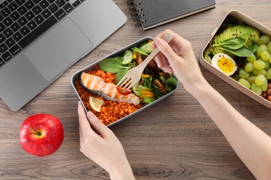 Photo of Woman eating healthy products high in vegetable fats near laptop at wooden table, top view