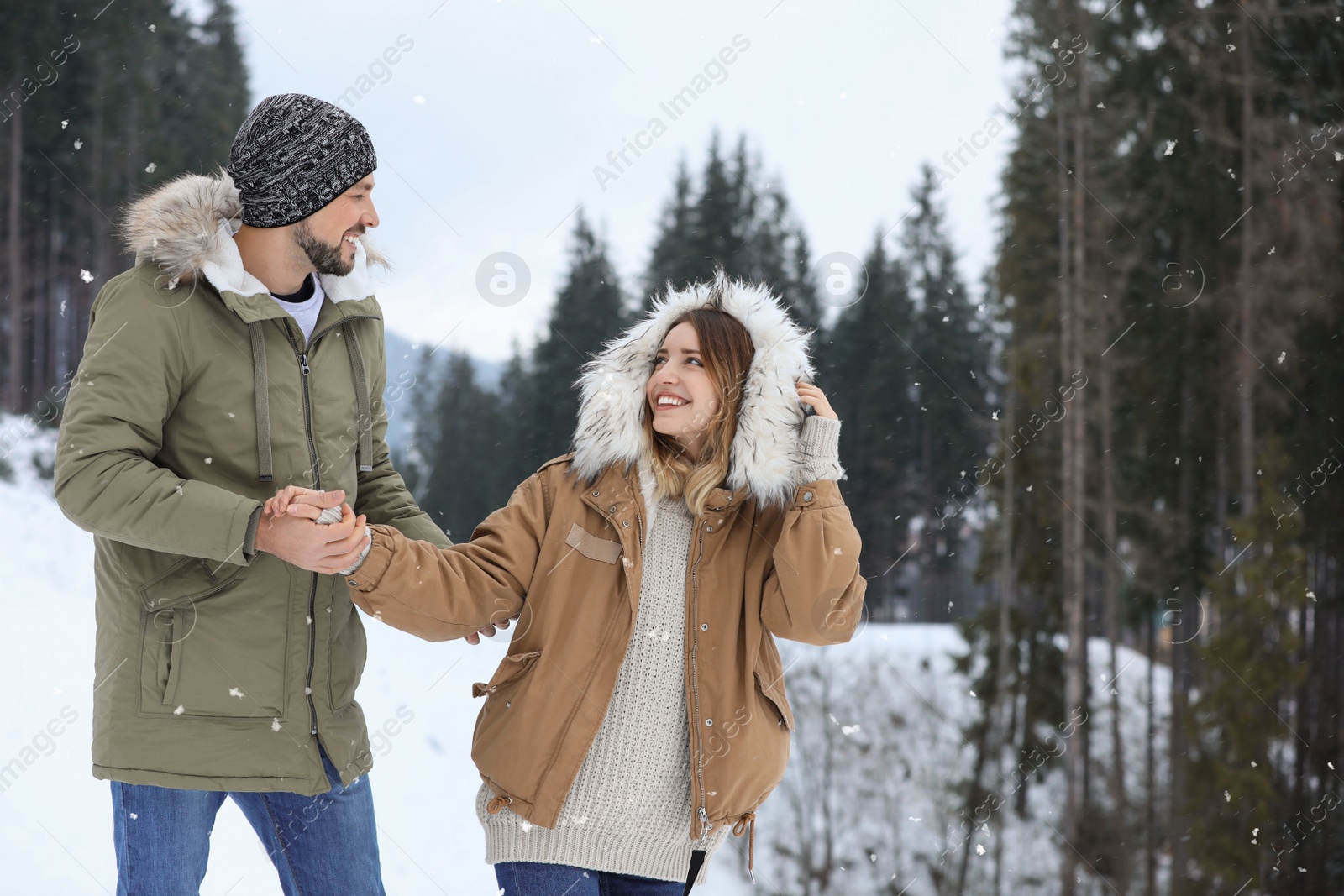 Photo of Happy couple near conifer forest on snowy day, space for text. Winter vacation