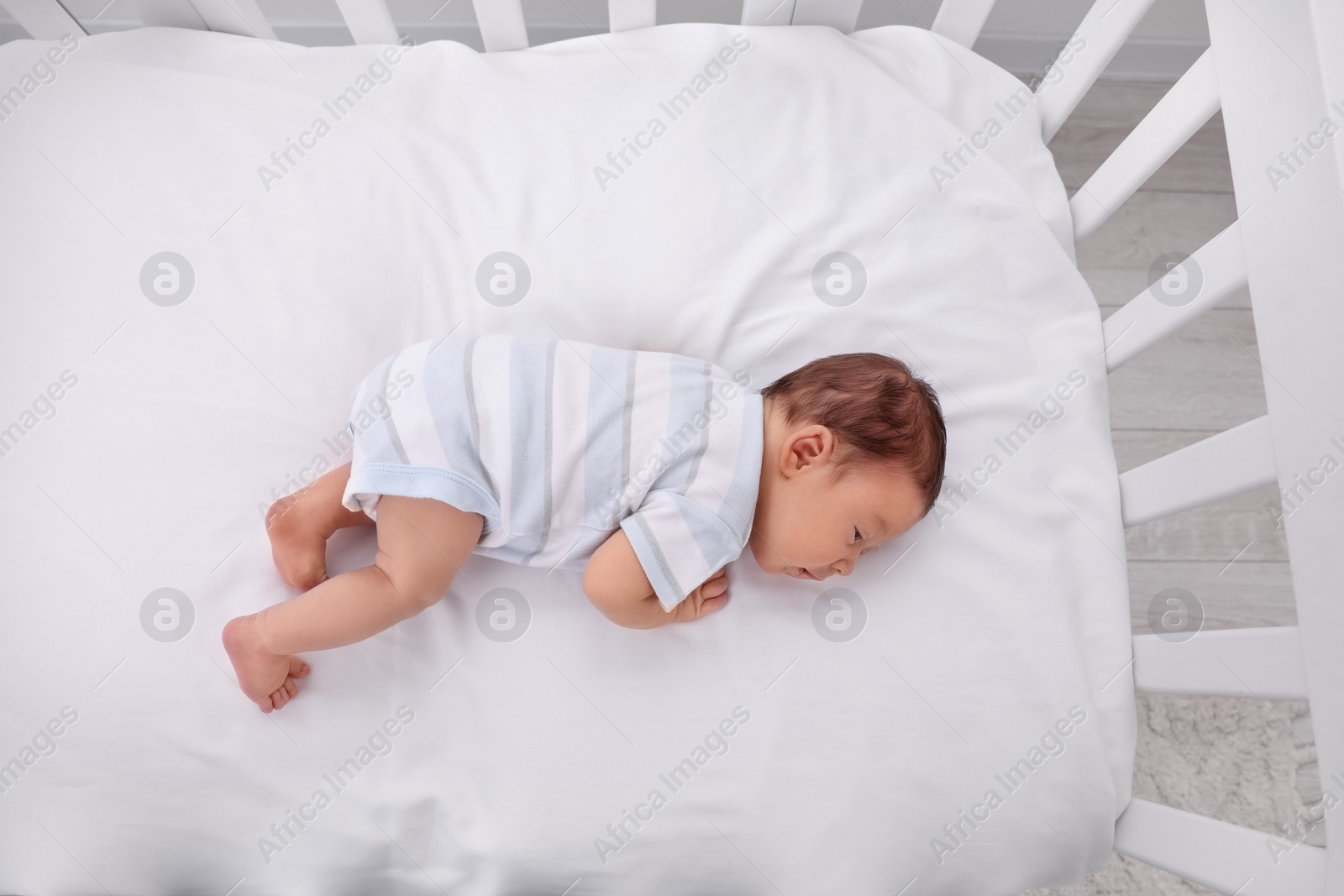 Photo of Cute newborn baby sleeping in crib, top view. Bedtime