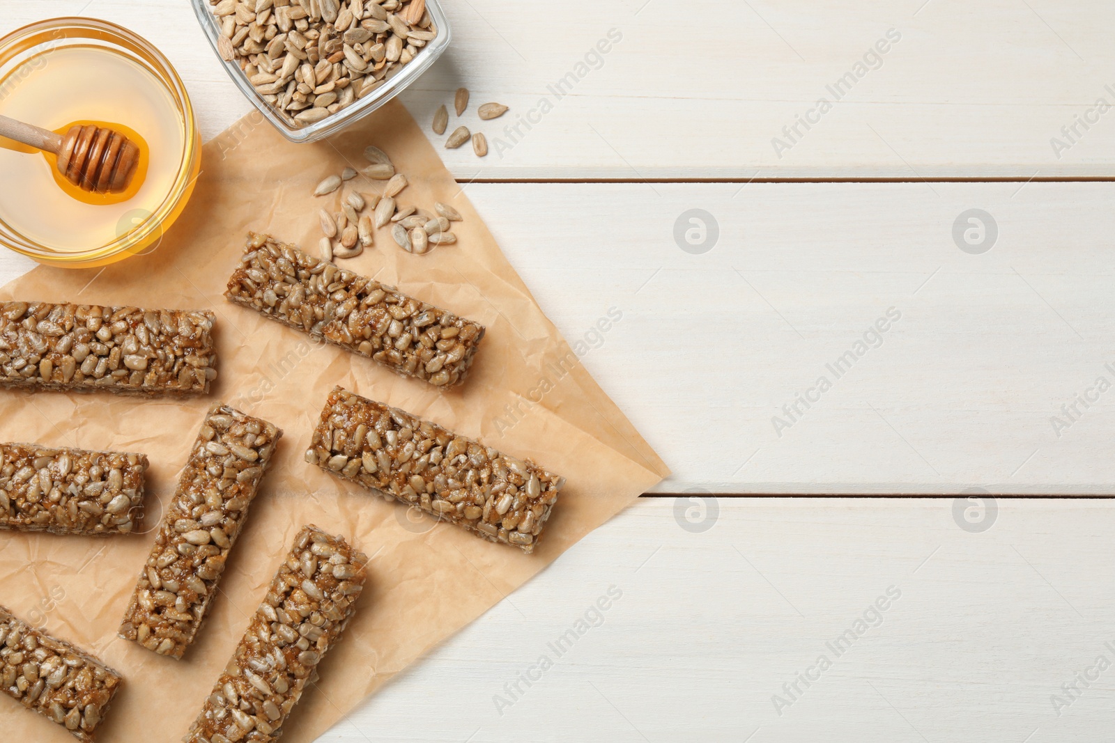 Photo of Delicious sweet kozinaki bars, honey and sunflower seeds on white wooden table, flat lay. Space for text