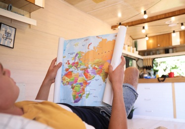 Photo of Young traveler with world map planning trip on bed in motorhome, closeup