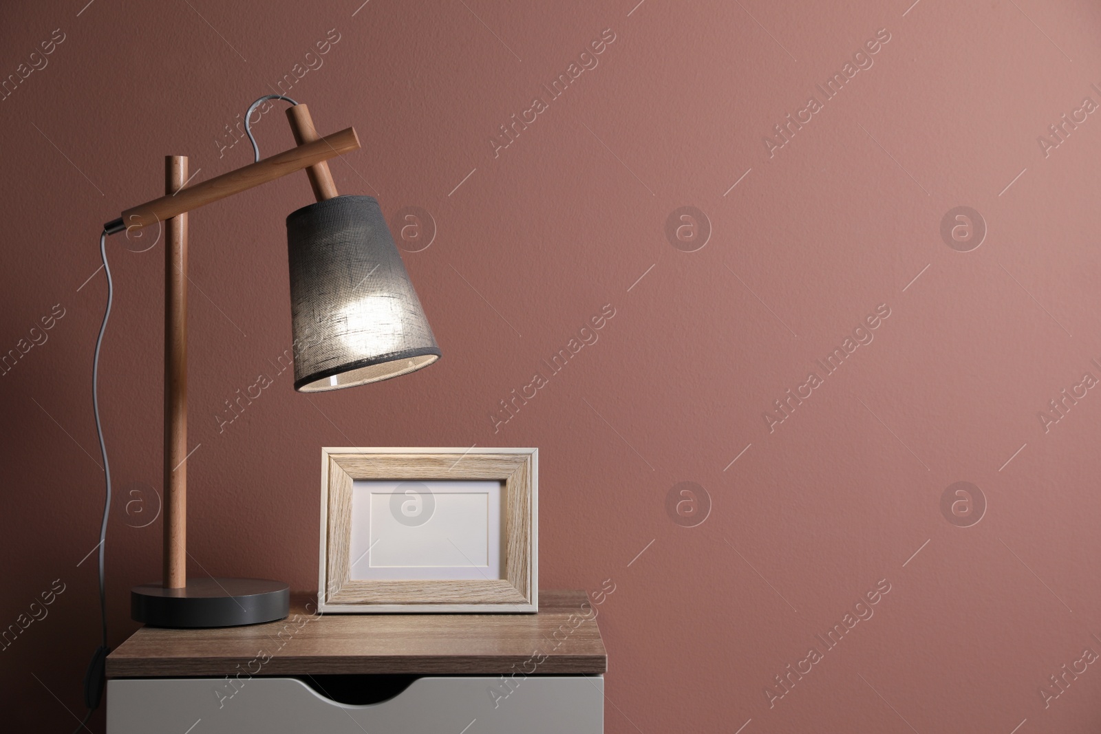 Photo of Wooden nightstand with frame and modern lamp in room, space for text