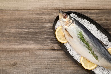 Plate with salted herring, rosemary and lemon on wooden table, top view. Space for text