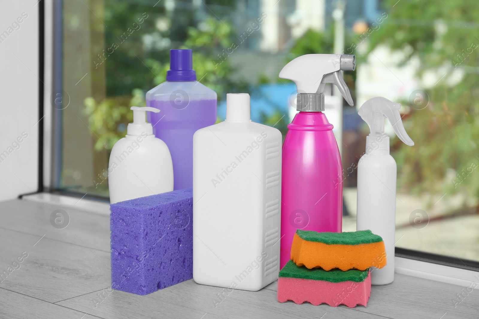 Photo of Many different bottles of detergents and sponges on window sill indoors. Cleaning supplies