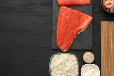 Photo of Making sushi rolls. Flat lay composition with fresh salmon and other ingredients on black wooden table. Space for text