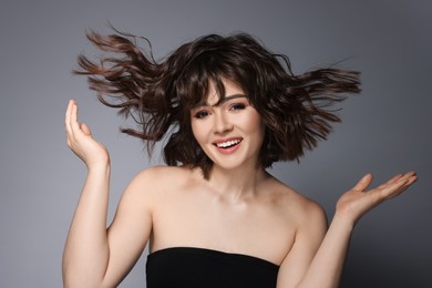 Portrait of beautiful young woman with wavy hairstyle on grey background