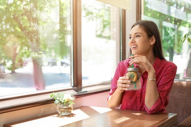 Young woman with mason jar of tasty natural lemonade in cafe. Detox drink