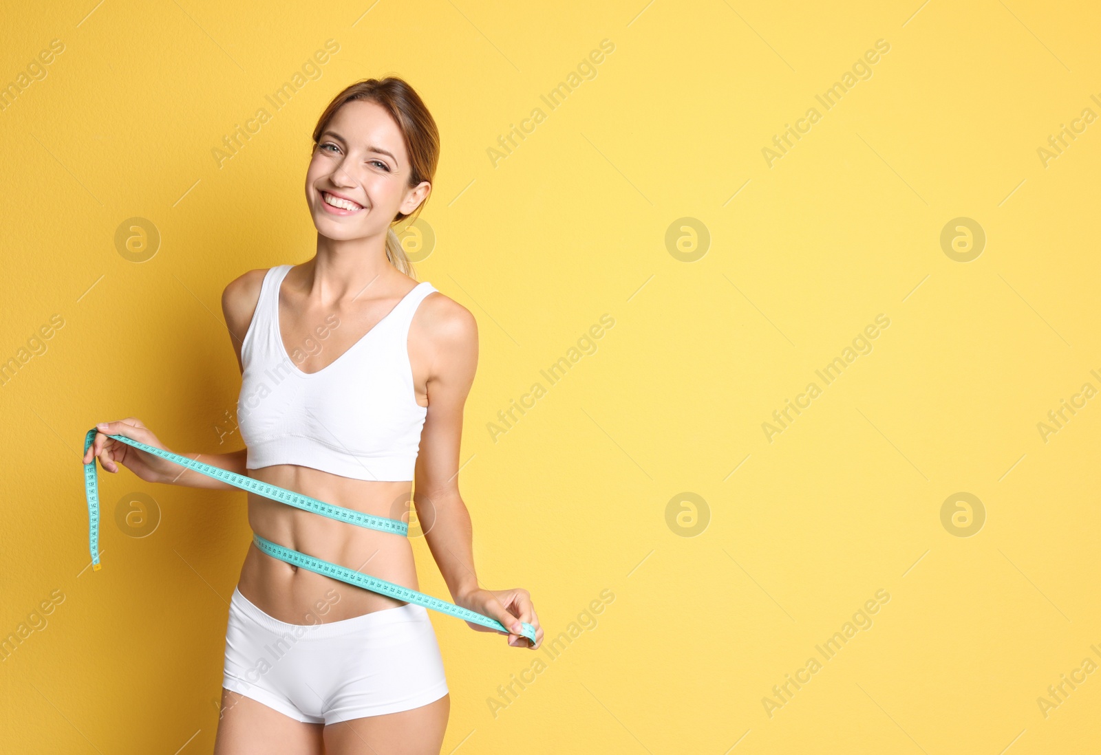 Photo of Happy slim woman in underwear with measuring tape on color background. Positive weight loss diet results