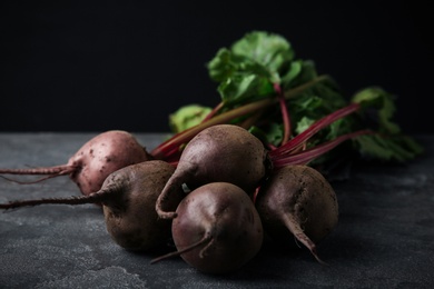 Photo of Bunch of fresh beets with leaves on grey table against black background. Space for text