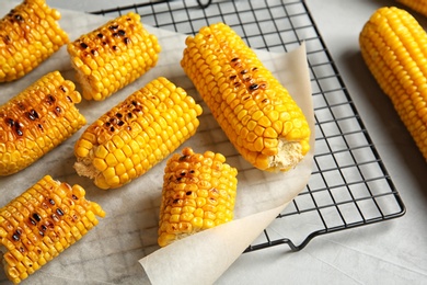 Photo of Cooling rack with grilled corn cobs on light background