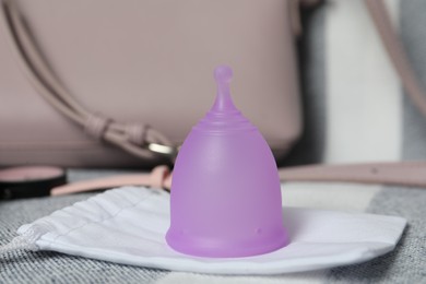 Violet menstrual cup with cotton bag on grey fabric, closeup