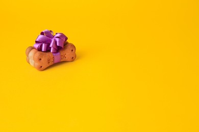 Bone shaped dog cookies with purple bow on yellow background. Space for text