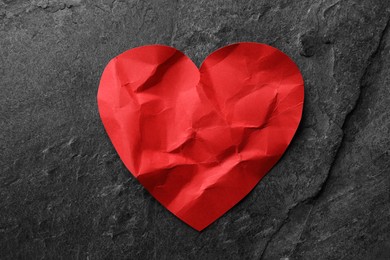 Photo of Crumpled red paper heart on dark grey table, top view. Broken heart