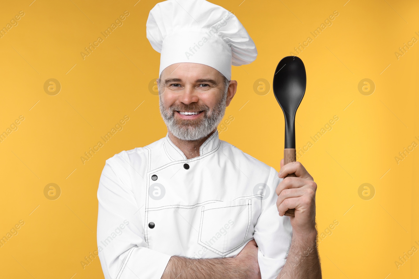 Photo of Happy chef in uniform with spoon on orange background