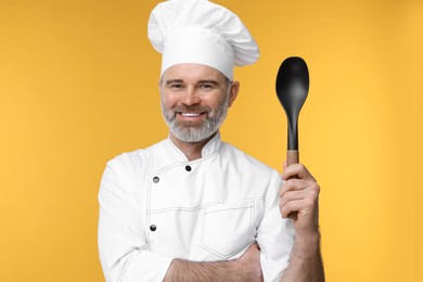 Happy chef in uniform with spoon on orange background