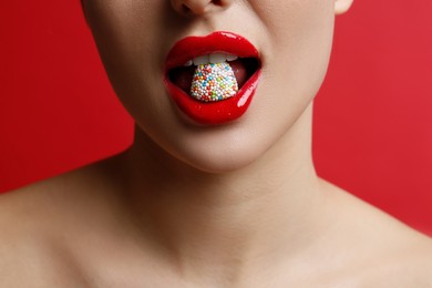 Photo of Closeup view of woman with beautiful lips eating candy on red background