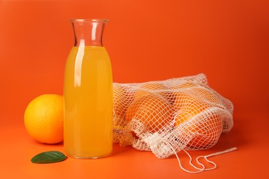 Photo of Net bag with fresh oranges and juice in bottle on color background, closeup