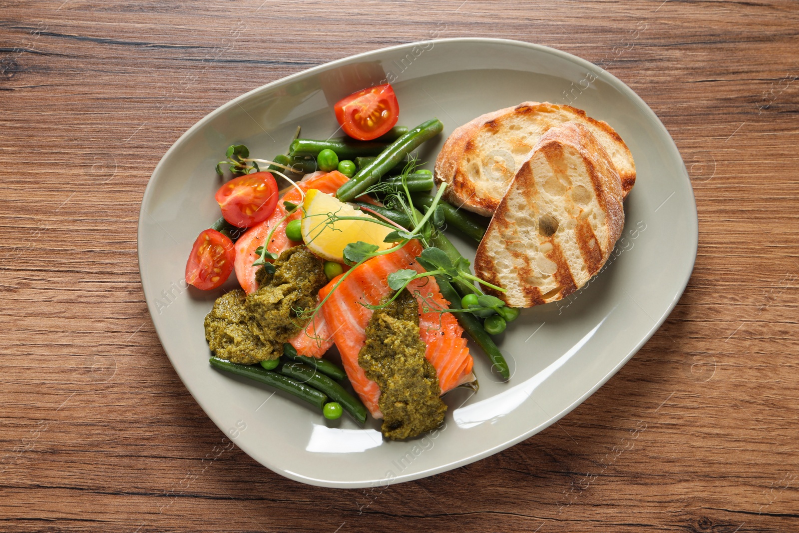 Photo of Tasty cooked salmon with pesto sauce on wooden table, top view