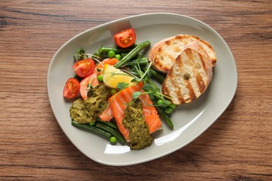 Photo of Tasty cooked salmon with pesto sauce on wooden table, top view