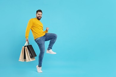 Photo of Excited man with many paper shopping bags on light blue background. Space for text