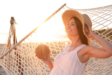 Photo of Young woman with tropical cocktail relaxing in hammock on beach at sunset