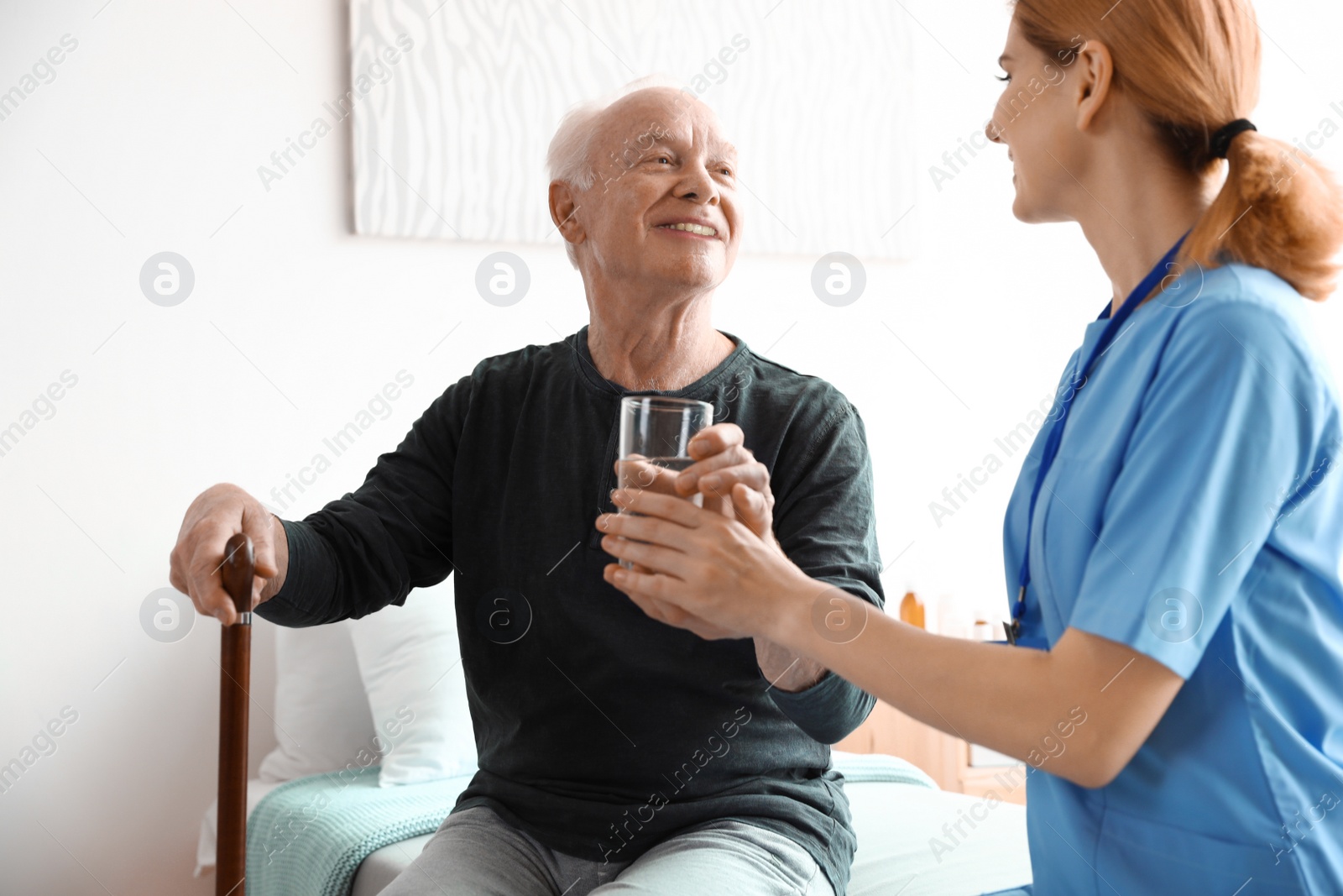 Photo of Nurse giving glass of water to elderly man indoors. Medical assistance