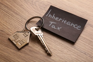 Photo of Inheritance Tax. Card and key with key chain in shape of house on wooden table, closeup