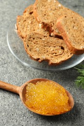 Photo of Fresh pike caviar in spoon and bread on grey table