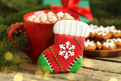 Photo of Tasty cookie in shape of Christmas stocking, cocoa with marshmallows and fir tree branch on wooden table, closeup. Space for text