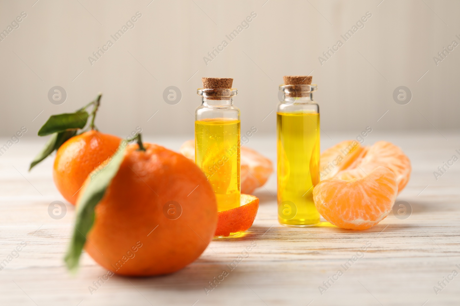 Photo of Bottles of tangerine essential oil, fresh fruits and peel on white wooden table