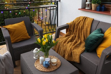Photo of Soft pillows, blanket, candles and yellow tulips on rattan garden furniture outdoors