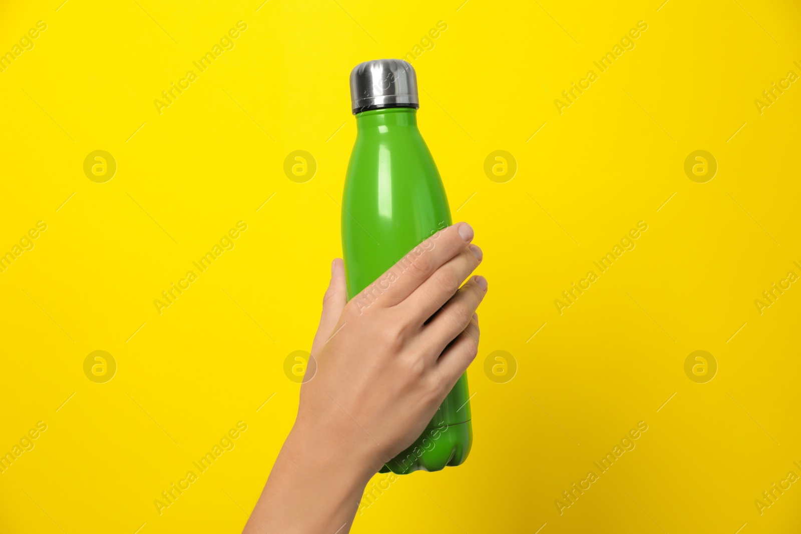 Photo of Woman holding modern green thermos on yellow background, closeup