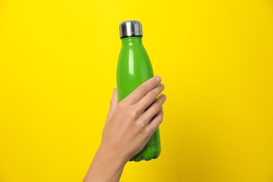 Woman holding modern green thermos on yellow background, closeup