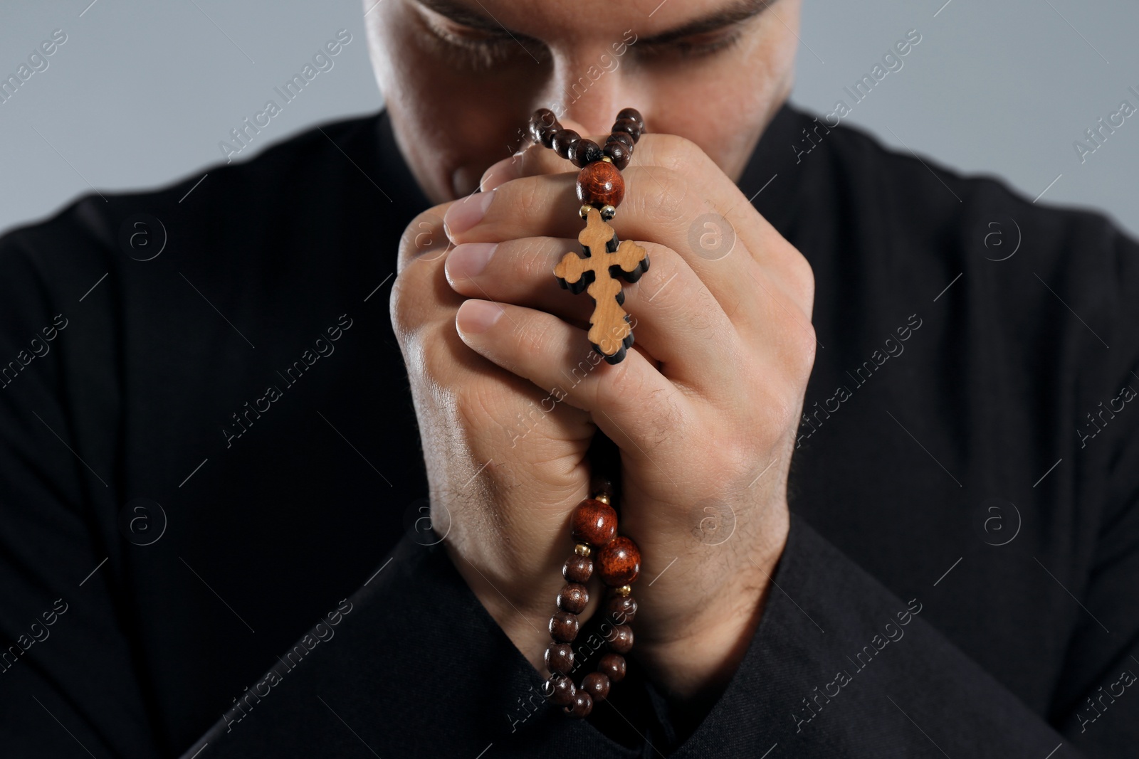 Photo of Priest with rosary beads praying on grey background, closeup