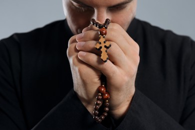 Photo of Priest with rosary beads praying on grey background, closeup