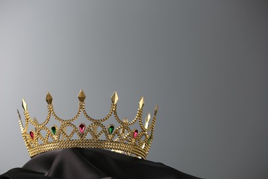 Beautiful golden crown with gems on dark cloth against grey background. Space for text