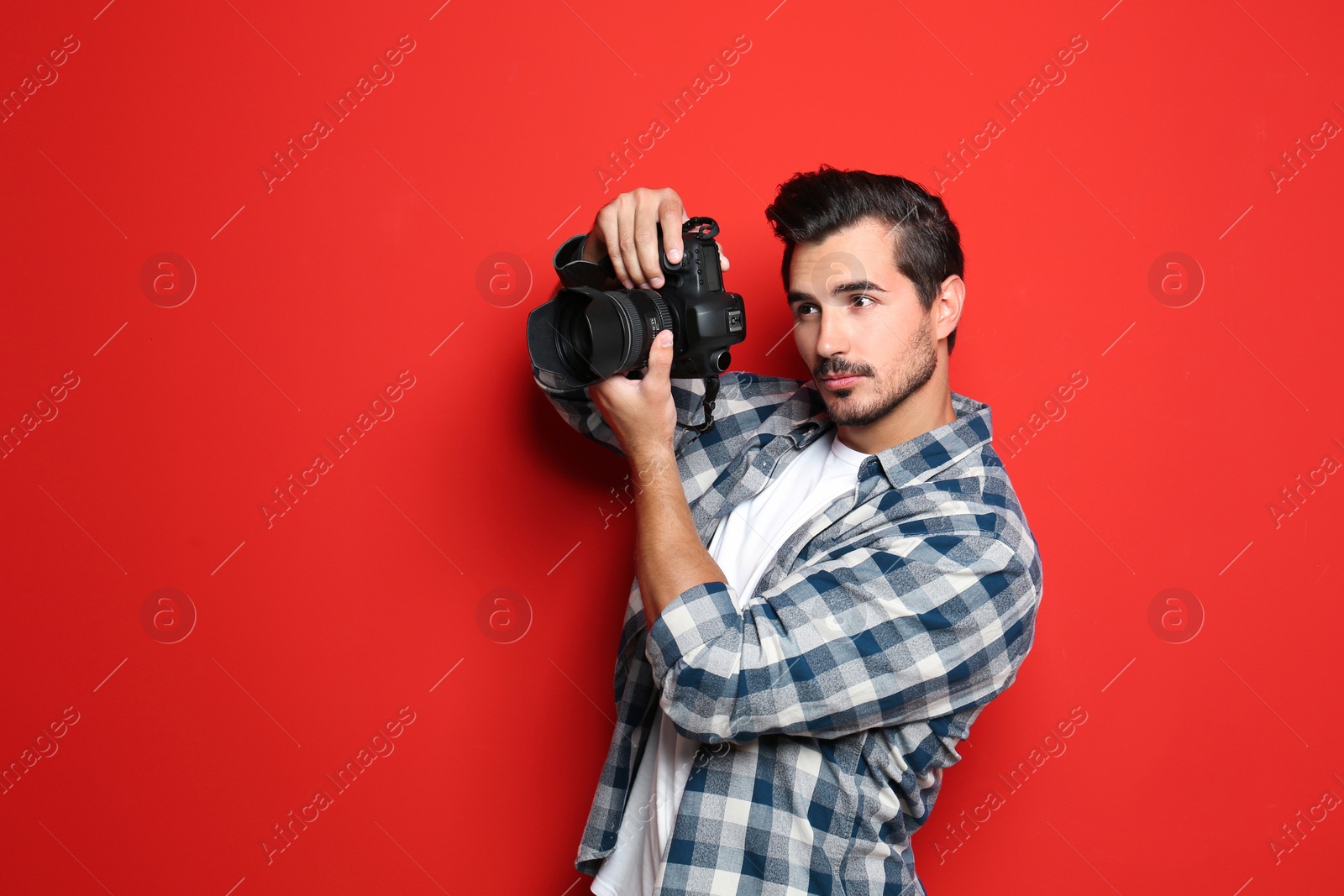 Photo of Young photographer with professional camera on red background. Space for text