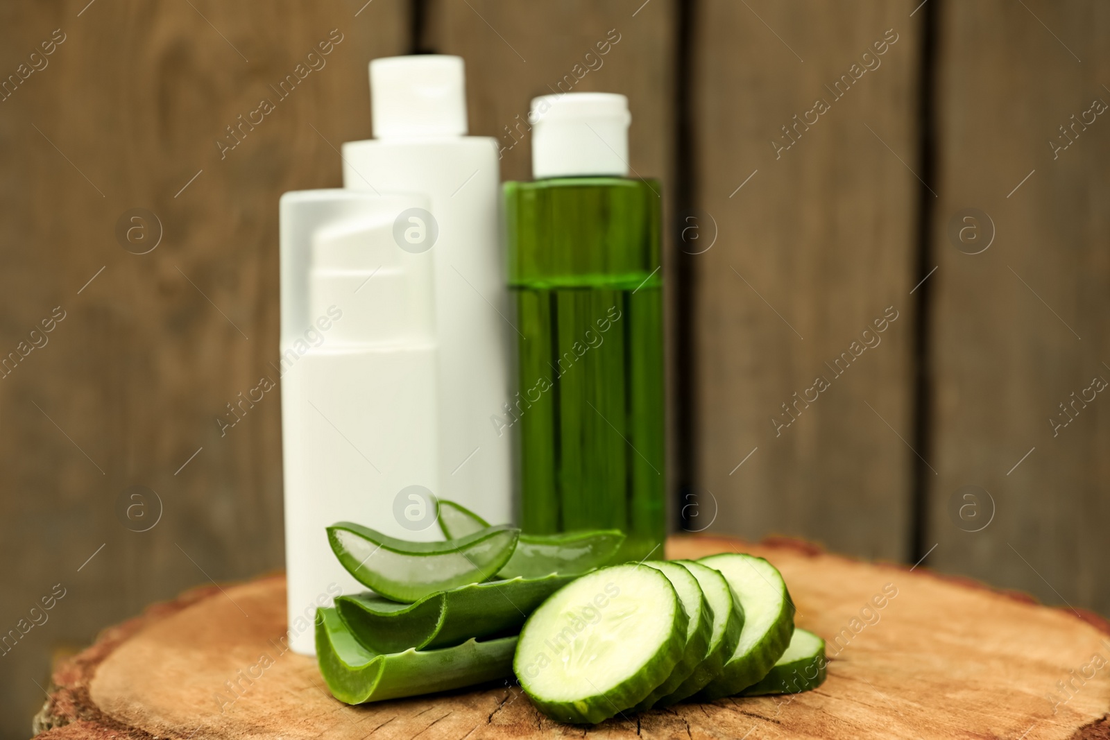 Photo of Bottles of cosmetic products, sliced aloe vera leaves and cucumber on wooden stump
